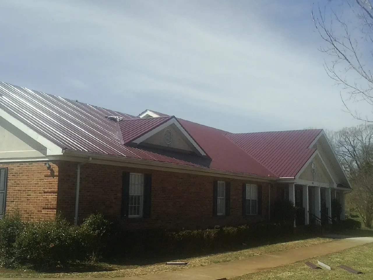 Red metal roof with gabled entries on a long brick building, from a Hail Damage Roof Repair job in Mount Ephraim