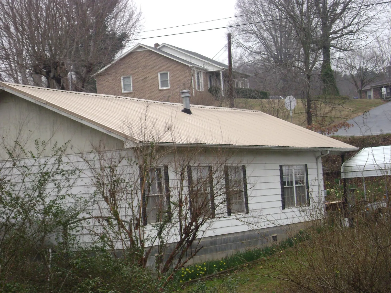 Tan metal roof on a white sided house set into a hillside — Commercial Roofing by Roofing Brothers in Mount Ephraim